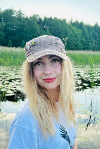 Катя в кепке с пином большая синица на фоне озера